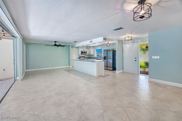 kitchen featuring a textured ceiling, ceiling fan with notable chandelier, light tile patterned floors, appliances with stainless steel finishes, and white cabinetry