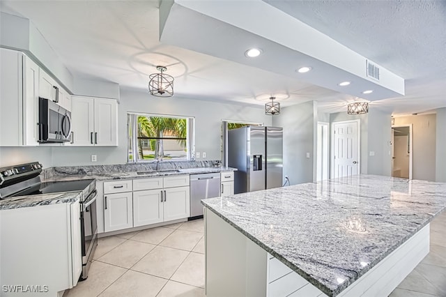 kitchen with appliances with stainless steel finishes, white cabinets, a kitchen island, light tile patterned flooring, and sink