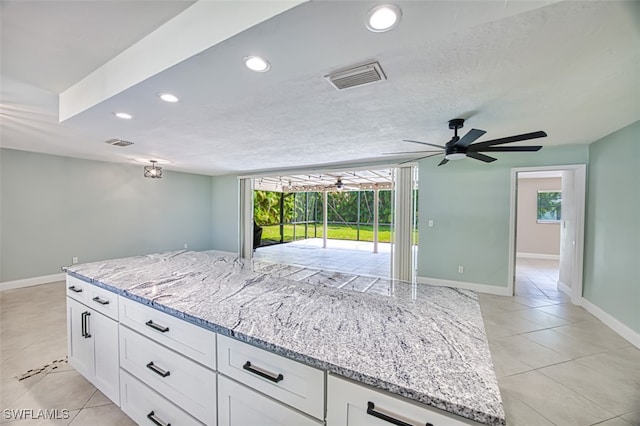 kitchen featuring light tile patterned flooring, white cabinets, light stone counters, and ceiling fan