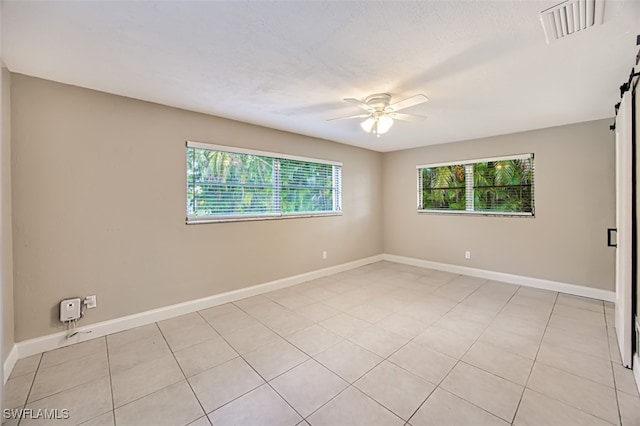 empty room featuring ceiling fan, a barn door, and light tile patterned flooring