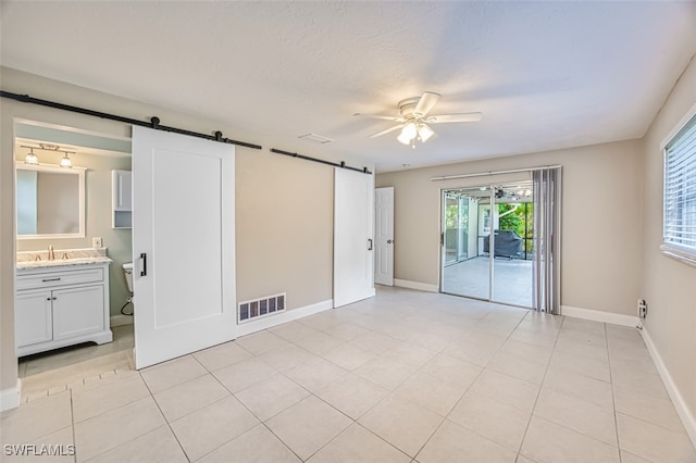 unfurnished room with ceiling fan, sink, a barn door, and light tile patterned floors