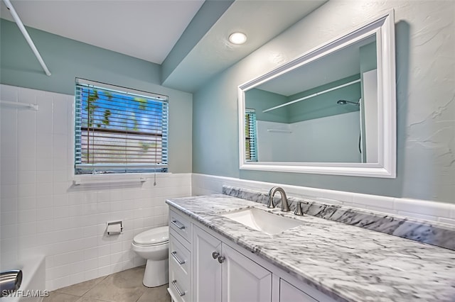 bathroom with wainscoting, toilet, tile patterned floors, vanity, and tile walls