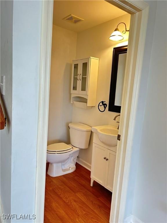 half bath featuring visible vents, toilet, vanity, wood finished floors, and baseboards