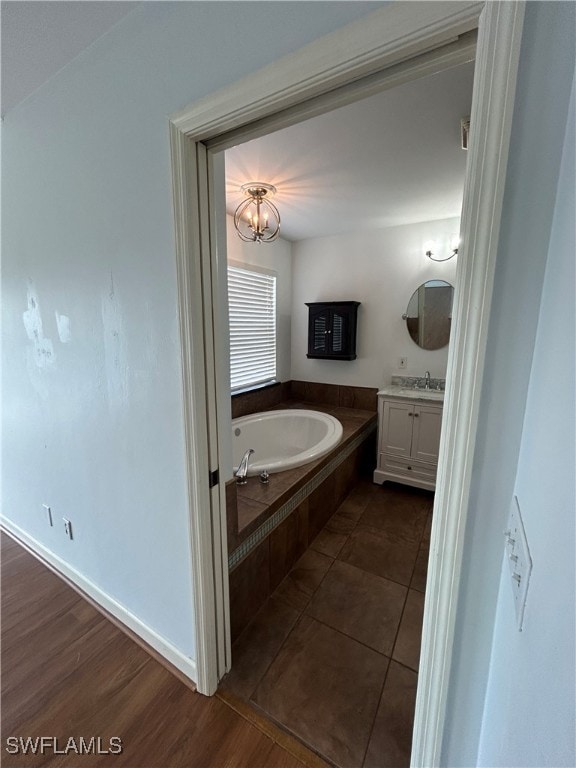 bathroom with hardwood / wood-style flooring, a relaxing tiled tub, and vanity