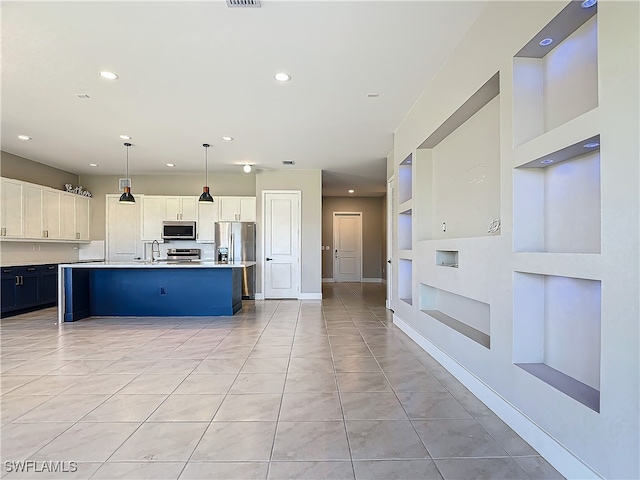 kitchen with hanging light fixtures, appliances with stainless steel finishes, an island with sink, and light countertops