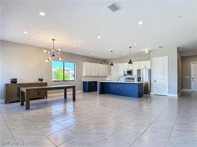 kitchen with white cabinets, decorative light fixtures, stainless steel appliances, and an island with sink