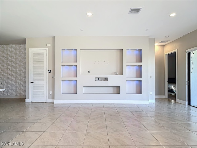 unfurnished living room with baseboards, visible vents, an accent wall, built in shelves, and recessed lighting