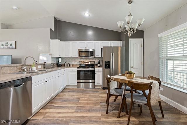 kitchen featuring lofted ceiling, light wood-type flooring, stainless steel appliances, and hanging light fixtures