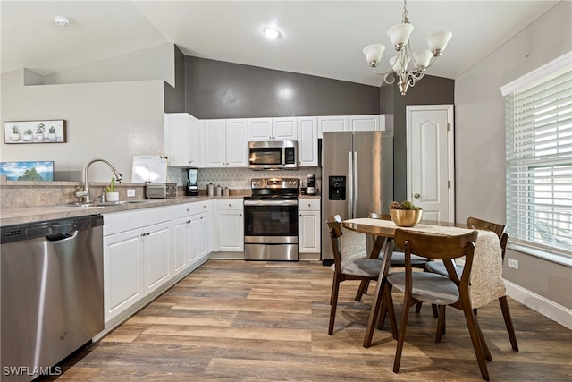 kitchen featuring lofted ceiling, hanging light fixtures, appliances with stainless steel finishes, sink, and an inviting chandelier