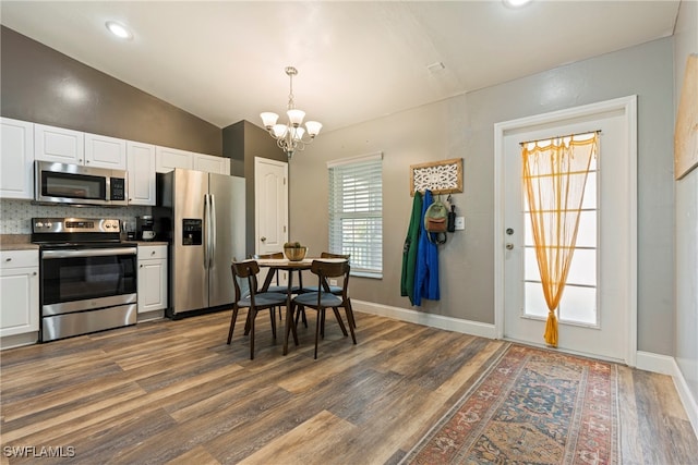 kitchen featuring white cabinetry, stainless steel appliances, wood-type flooring, and vaulted ceiling