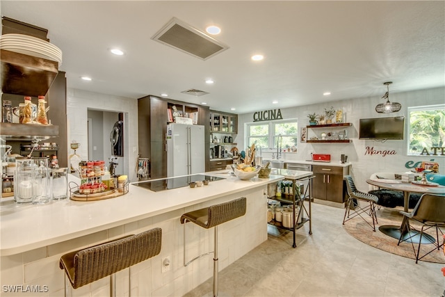 kitchen with decorative light fixtures, white refrigerator, light tile patterned flooring, black electric stovetop, and a breakfast bar