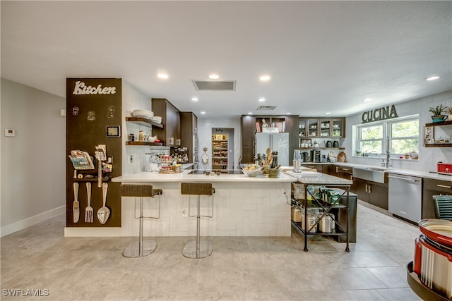 kitchen featuring white fridge, dark brown cabinets, a kitchen bar, sink, and stainless steel dishwasher