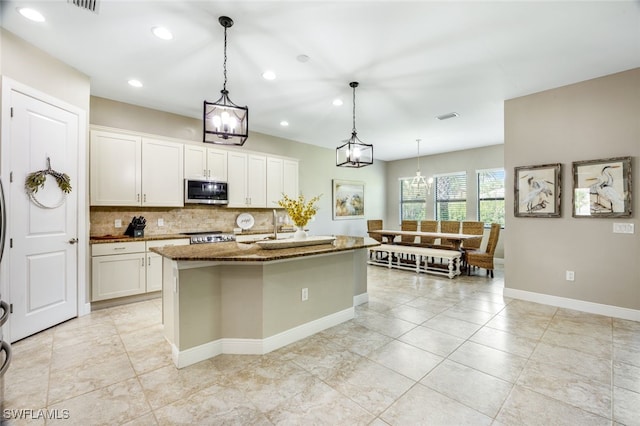 kitchen featuring backsplash, white cabinets, an island with sink, and decorative light fixtures