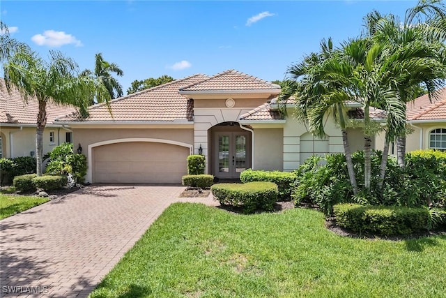 mediterranean / spanish home with a tiled roof, stucco siding, french doors, decorative driveway, and an attached garage