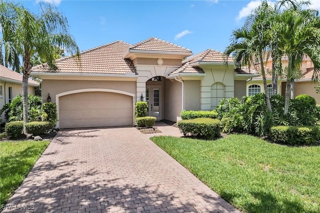 mediterranean / spanish house featuring stucco siding, a front lawn, a garage, a tile roof, and decorative driveway