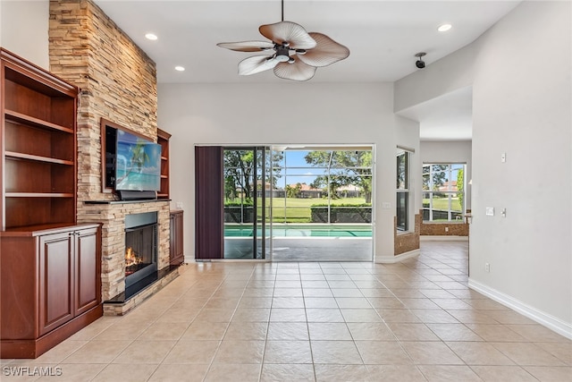 unfurnished living room featuring ceiling fan, light tile patterned floors, and a stone fireplace