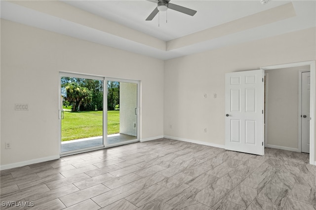 tiled empty room featuring ceiling fan, plenty of natural light, and a tray ceiling