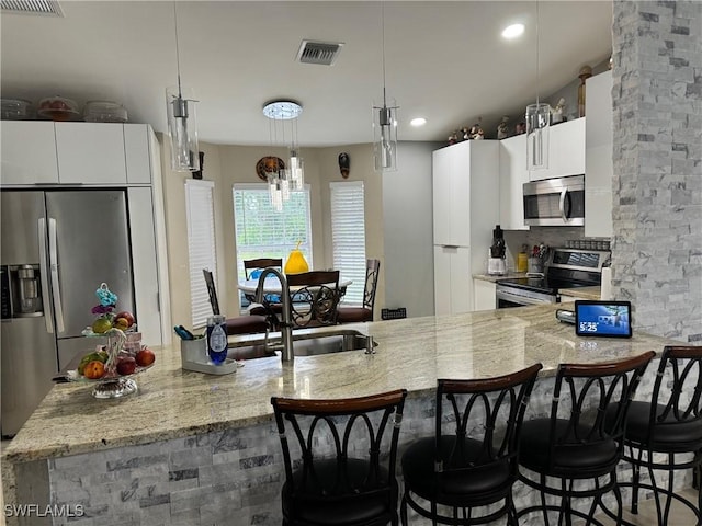 kitchen featuring decorative light fixtures, sink, white cabinets, a kitchen breakfast bar, and stainless steel appliances