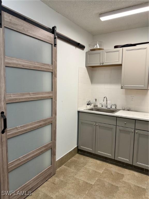 kitchen with sink, gray cabinets, backsplash, a textured ceiling, and a barn door