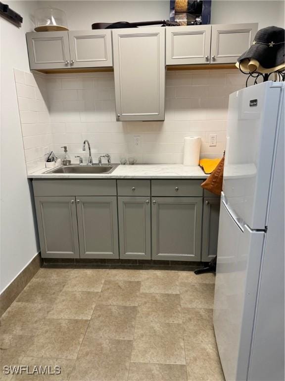 kitchen featuring backsplash, sink, white fridge, and gray cabinetry