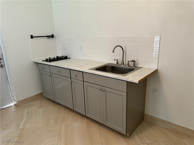 kitchen with black gas cooktop, tasteful backsplash, sink, gray cabinetry, and light stone countertops