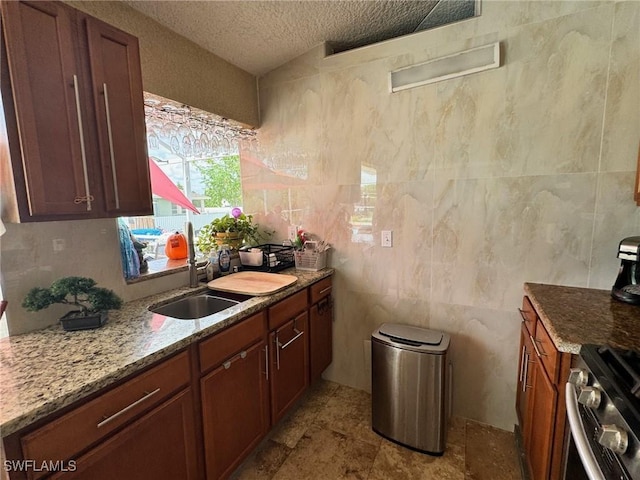 kitchen featuring sink, light stone counters, a textured ceiling, tile walls, and stainless steel range