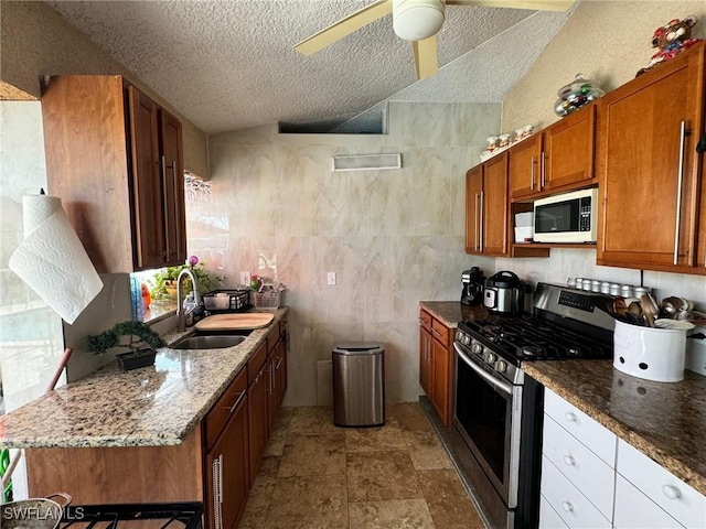 kitchen featuring sink, ceiling fan, light stone counters, gas stove, and a textured ceiling