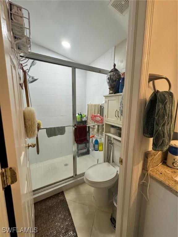 bathroom featuring toilet, a shower with shower door, and tile patterned flooring