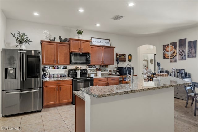 kitchen featuring arched walkways, light tile patterned floors, visible vents, brown cabinets, and black appliances