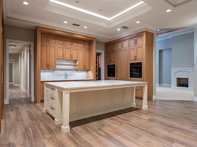 kitchen with a large island, decorative backsplash, a raised ceiling, black oven, and light wood-type flooring