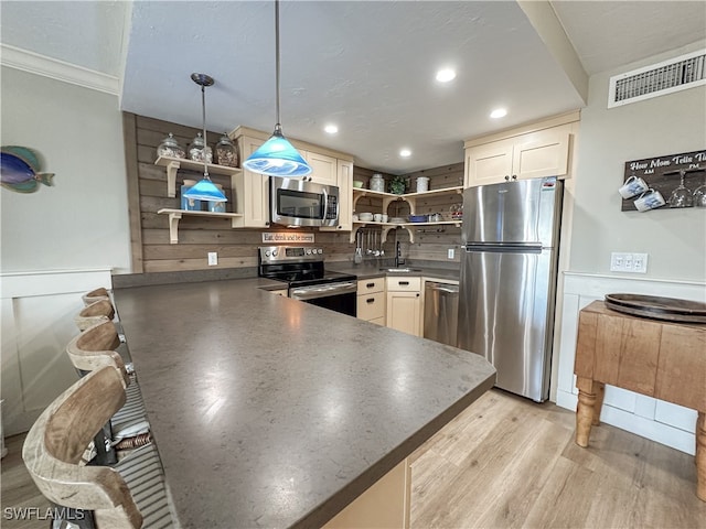 kitchen featuring stainless steel appliances, hanging light fixtures, light hardwood / wood-style floors, ornamental molding, and sink