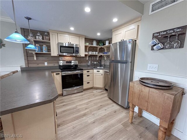 kitchen featuring stainless steel appliances, pendant lighting, cream cabinets, sink, and light hardwood / wood-style flooring