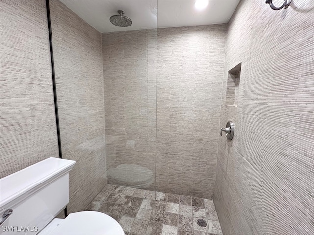 bathroom with a tile shower, tile walls, and toilet