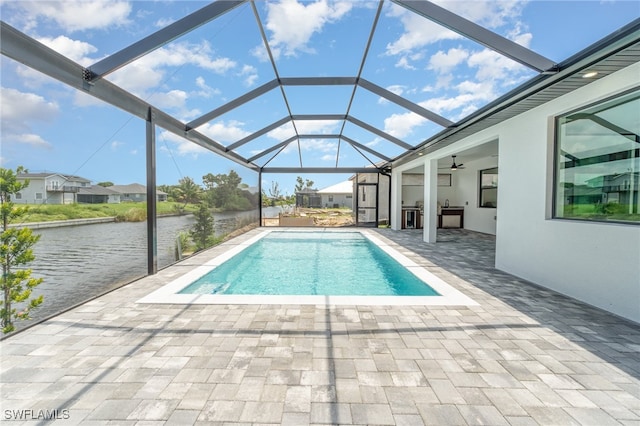 view of pool with glass enclosure, ceiling fan, a water view, and a patio