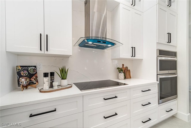 kitchen featuring white cabinets, stainless steel double oven, wall chimney range hood, and black electric stovetop