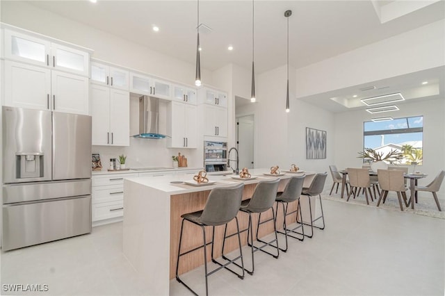 kitchen featuring pendant lighting, a center island with sink, white cabinets, wall chimney exhaust hood, and stainless steel fridge