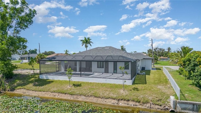 back of property featuring a water view, a patio area, glass enclosure, and a lawn