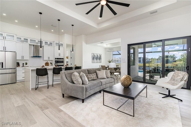 living room with a raised ceiling, a towering ceiling, ceiling fan, and light hardwood / wood-style flooring