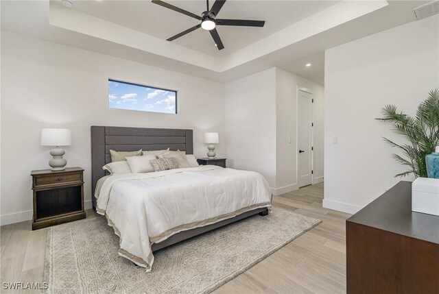 bedroom featuring a raised ceiling, ceiling fan, and light wood-type flooring