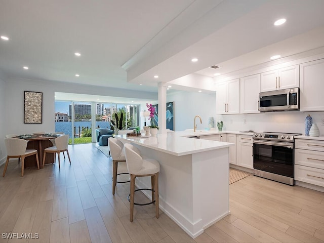 kitchen with a breakfast bar, sink, kitchen peninsula, stainless steel appliances, and white cabinets