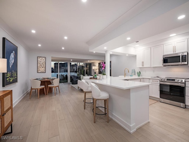 kitchen featuring appliances with stainless steel finishes, white cabinetry, sink, a kitchen bar, and kitchen peninsula