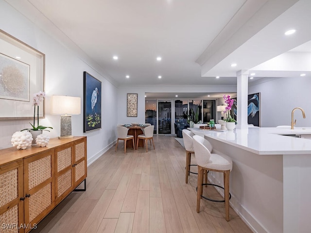 kitchen with sink, a breakfast bar area, ornate columns, kitchen peninsula, and light hardwood / wood-style floors