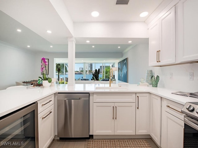 kitchen with white cabinetry, appliances with stainless steel finishes, beverage cooler, and kitchen peninsula