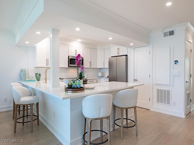 kitchen with light hardwood / wood-style flooring, a breakfast bar, stainless steel appliances, white cabinets, and kitchen peninsula