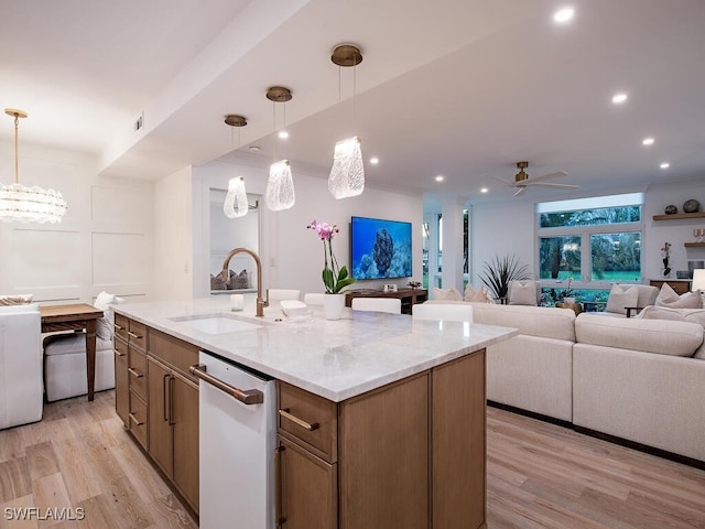 kitchen with sink, an island with sink, light hardwood / wood-style floors, ceiling fan with notable chandelier, and dishwasher