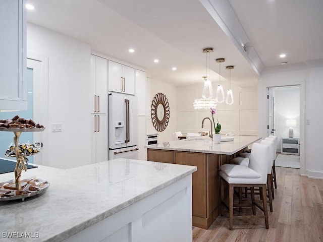 kitchen with pendant lighting, high end white fridge, white cabinetry, light stone counters, and a center island with sink