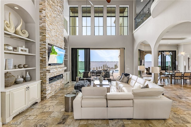 living room featuring a stone fireplace, a towering ceiling, built in features, and ceiling fan