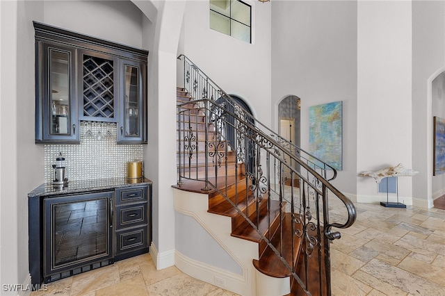 614 Coral Dr, Cape Coral, FL 33904 - stairs featuring a towering ceiling, baseboards, stone tile flooring, a bar, and arched walkways