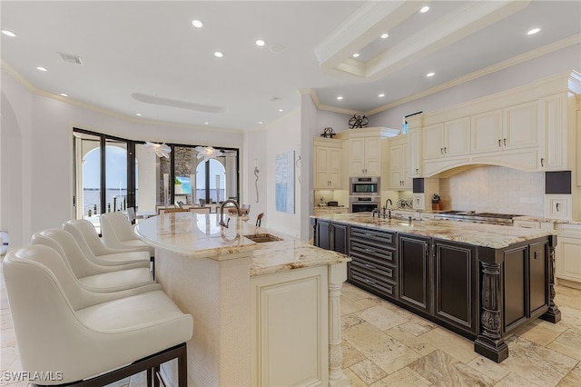 kitchen featuring light stone countertops, tasteful backsplash, a large island with sink, and crown molding