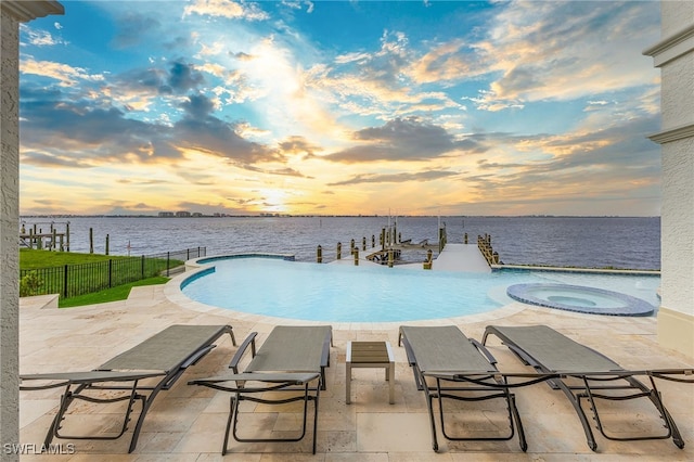 pool at dusk with a patio, a water view, and an in ground hot tub